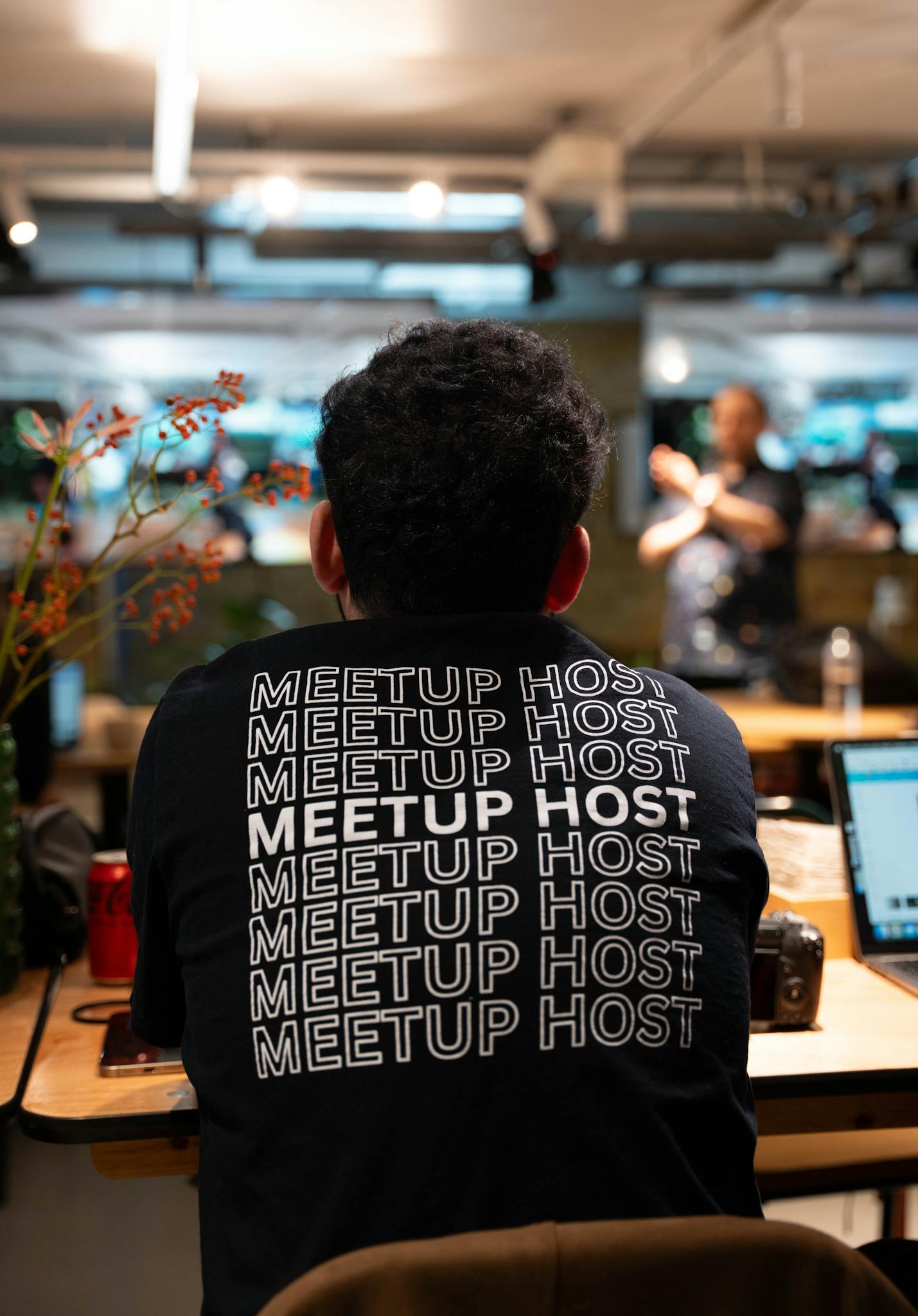 Man wearing 'MEETUP HOST' shirt at an informal networking event indoors.